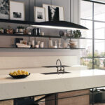 A modern kitchen island features a sleek faucet and a bowl of lemons, surrounded by minimalist open shelves with framed photos and assorted kitchenware, set against large windows.