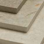 Four stacked stone slabs rest atop each other, displaying varied shades of beige with subtle veining. The stacked formation highlights their thickness and texture, emphasizing use in construction or decoration.