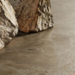 Rough textured rocks rest on a smooth, polished concrete surface, creating a contrast between natural and man-made elements. The environment appears minimal and serene.