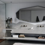Elegant bathroom interior with gray Caesarstone quartz countertop, double sinks, brass fittings, and a large angular mirror above the vanity.