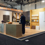 Modern exhibition booth showcasing tiles and wall decor with a visitor observing the displays.