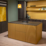 Modern kitchen with mustard yellow island, dark cabinets, open shelves, pendant light, and folded chairs.