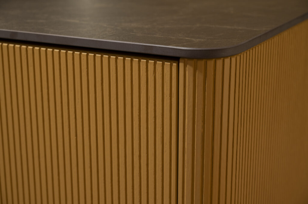 Corner of a wooden cabinet with vertical grooves and a dark, smooth countertop.
