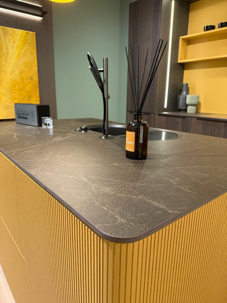 Modern kitchen island with dark countertop, sleek faucet, reed diffuser, and wooden paneling.