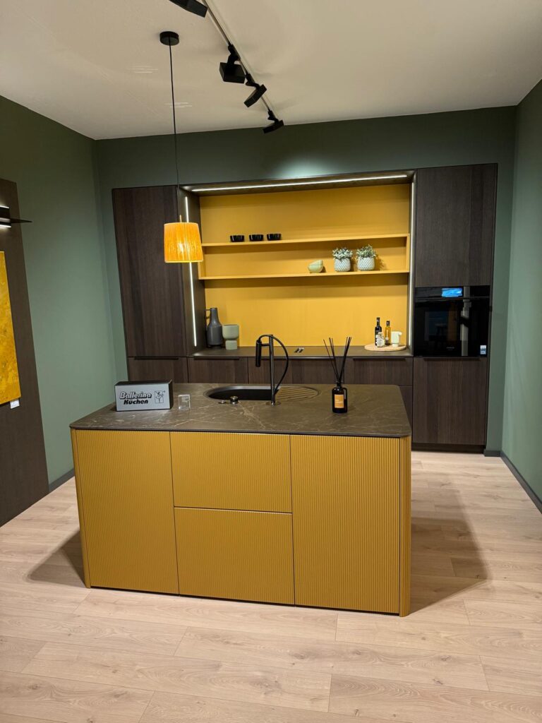Modern kitchen with mustard yellow island, dark cabinetry, pendant light, and decorative plants.
